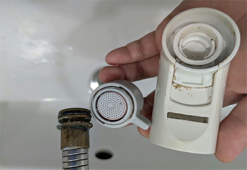 蛇口のシャワーヘッドを分解し、水垢や汚れがついた内部パーツを確認している様子